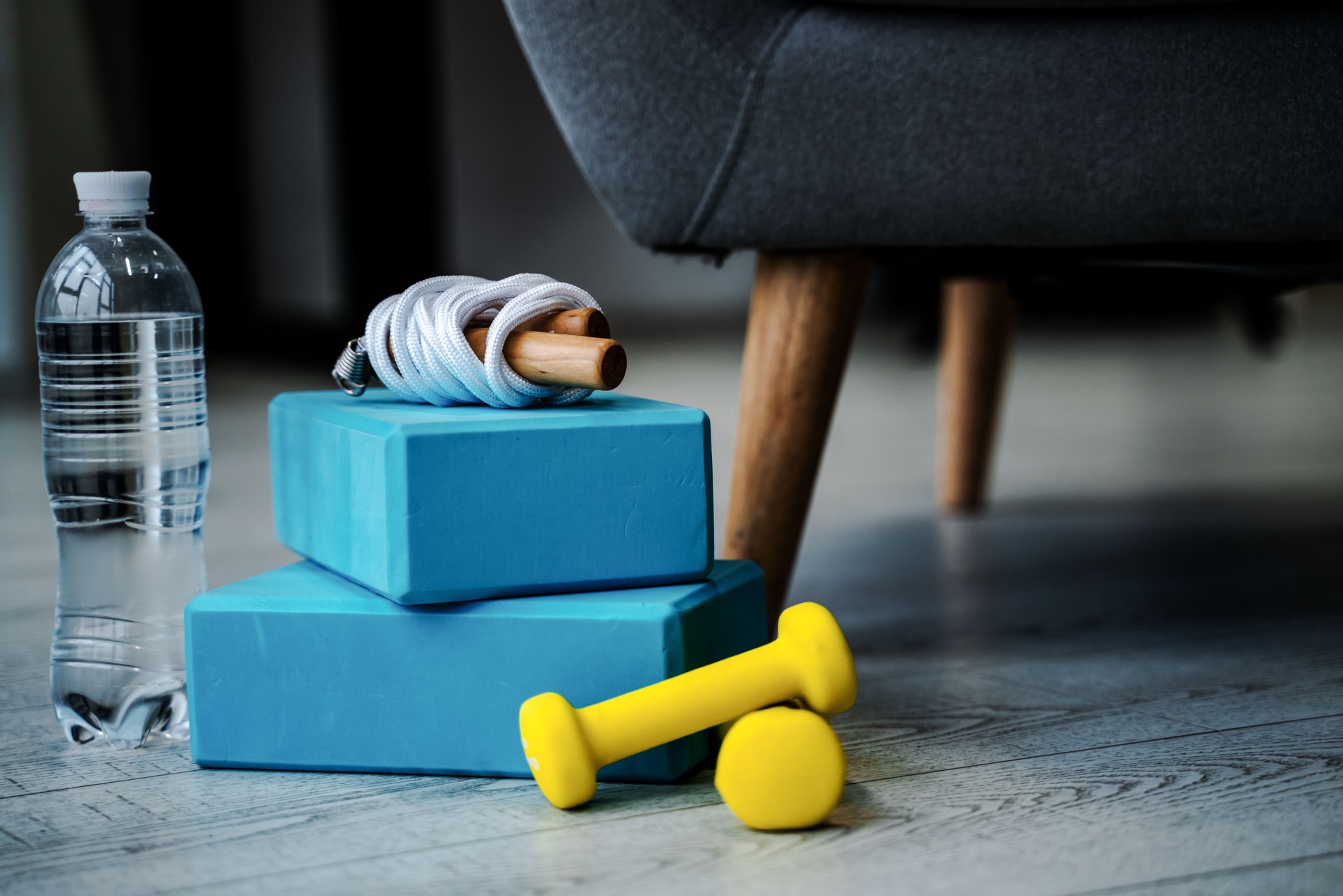 Sports equipment lies on the floor of the house, yellow dumbbells and bricks for push-ups, a jump rope and a bottle of water for training at home. Healthy and sporty lifestyle concept