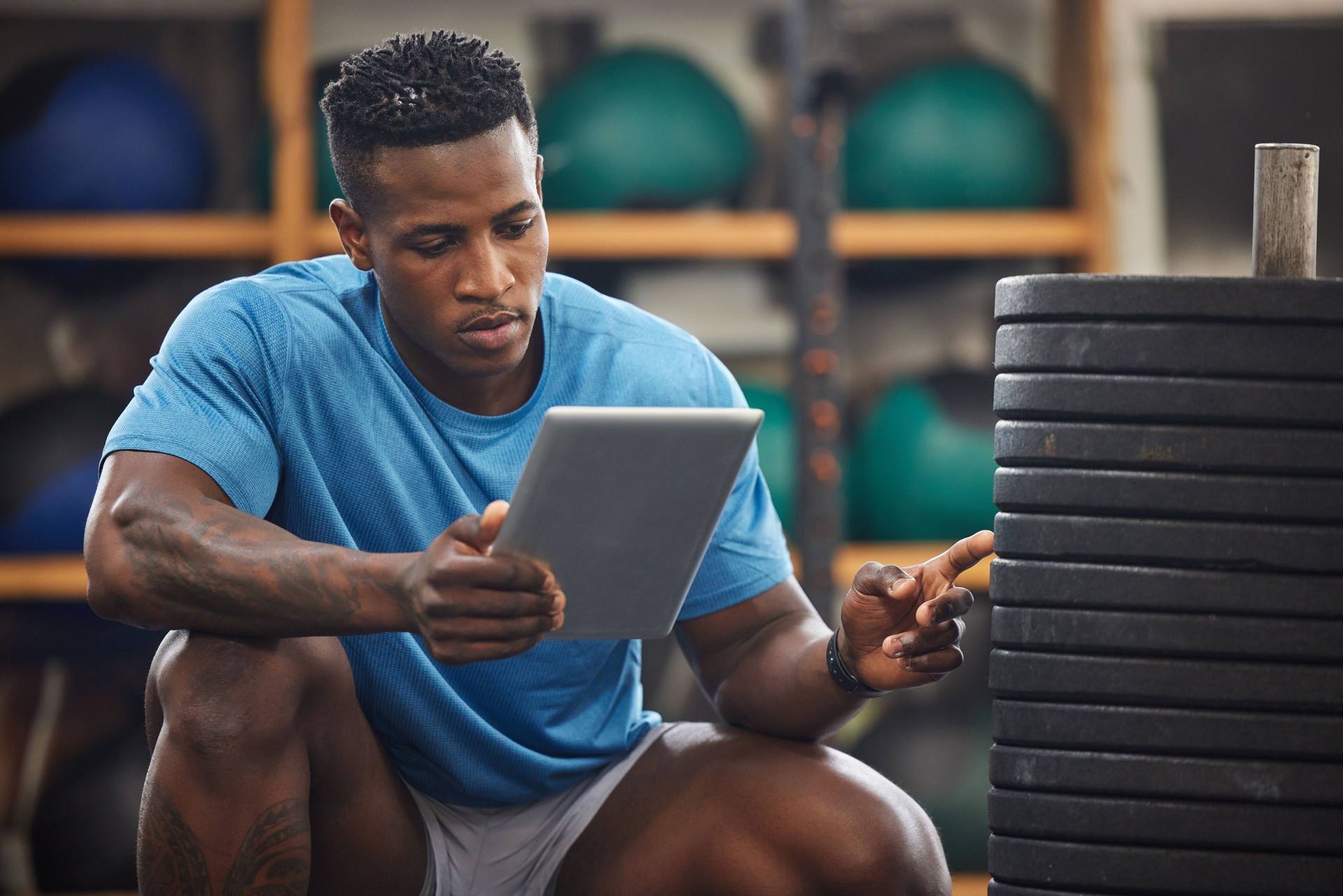Shot of a muscular young man using a digital tablet while checking equipment in a gym